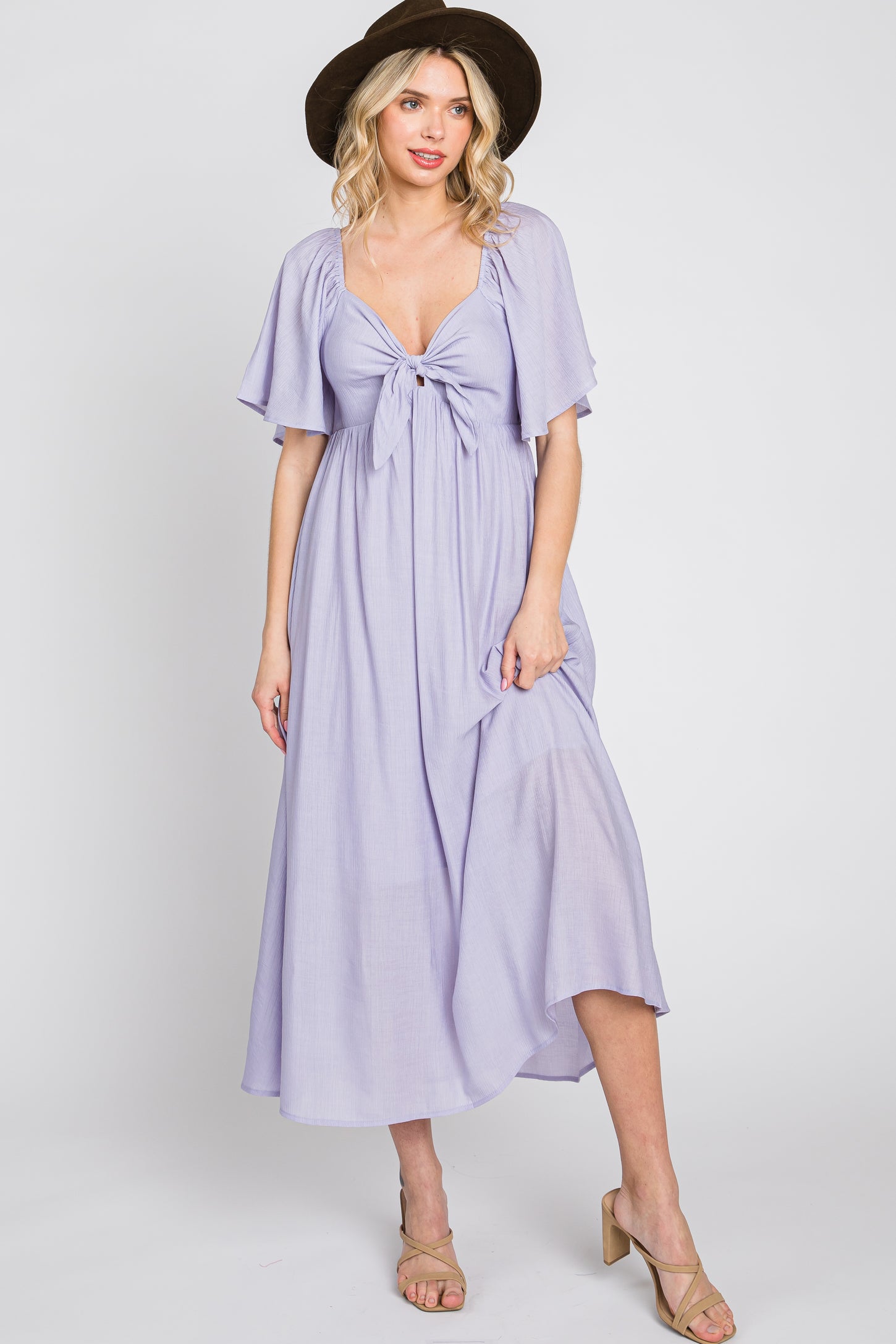 woman wearing a lavender midi dress with flutter sleeves and a knotted front, paired with a wide-brimmed hat and heels