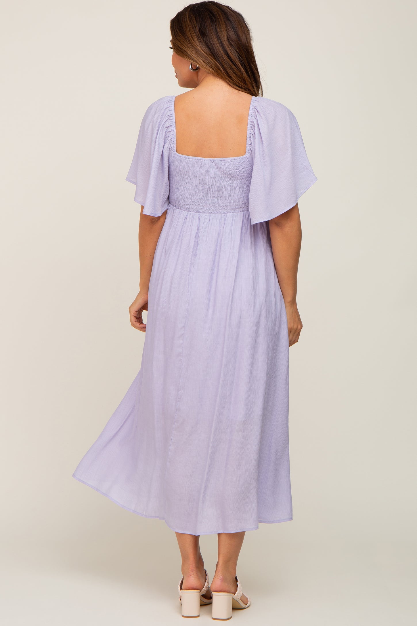 woman wearing a lilac maternity maxi dress with flutter sleeves and a smocked bodice, showing her back