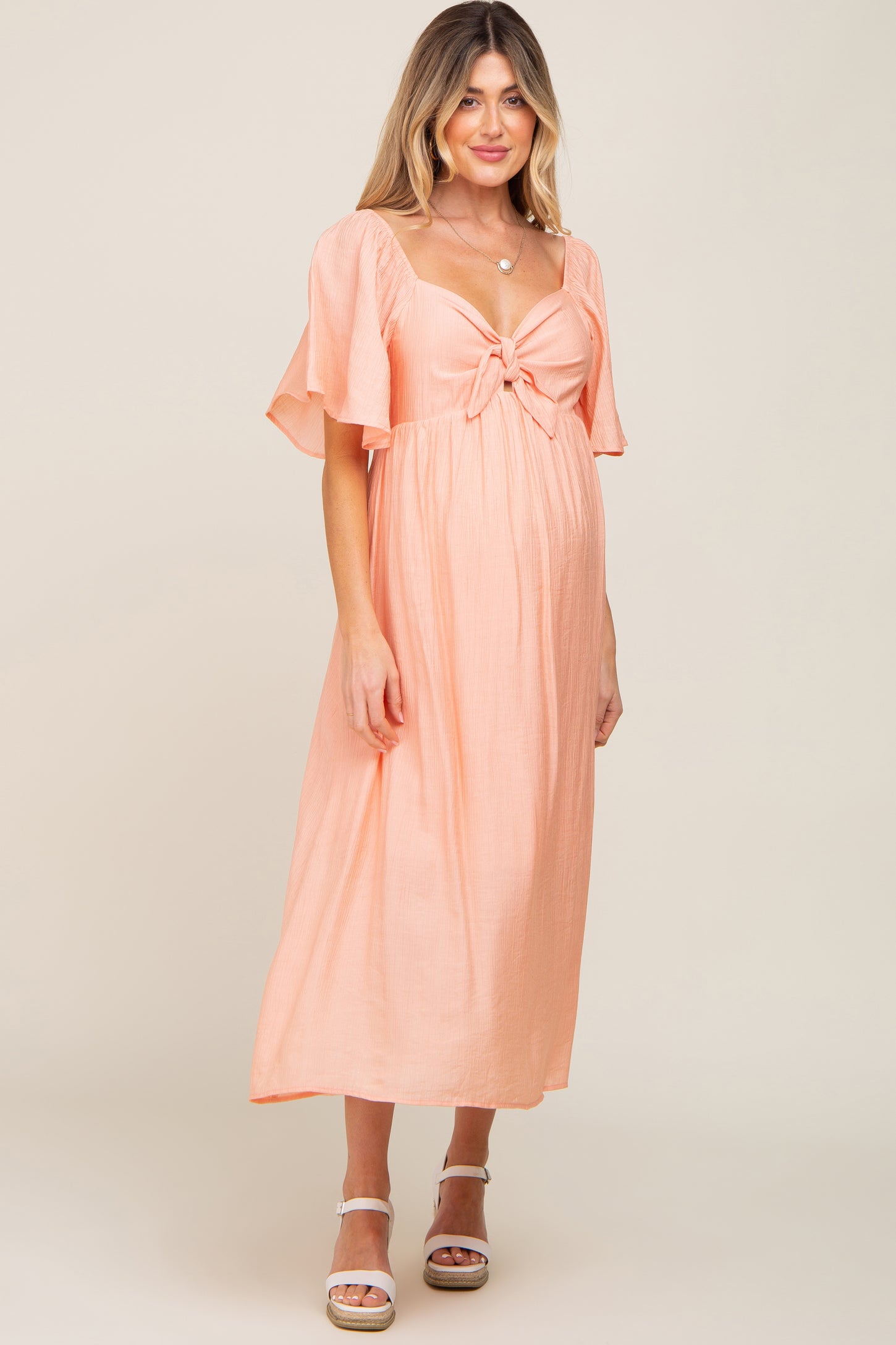 pregnant woman wearing a peach midi maternity dress with tie front and flutter sleeves