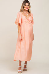 pregnant woman wearing a peach midi maternity dress with tie front and flutter sleeves