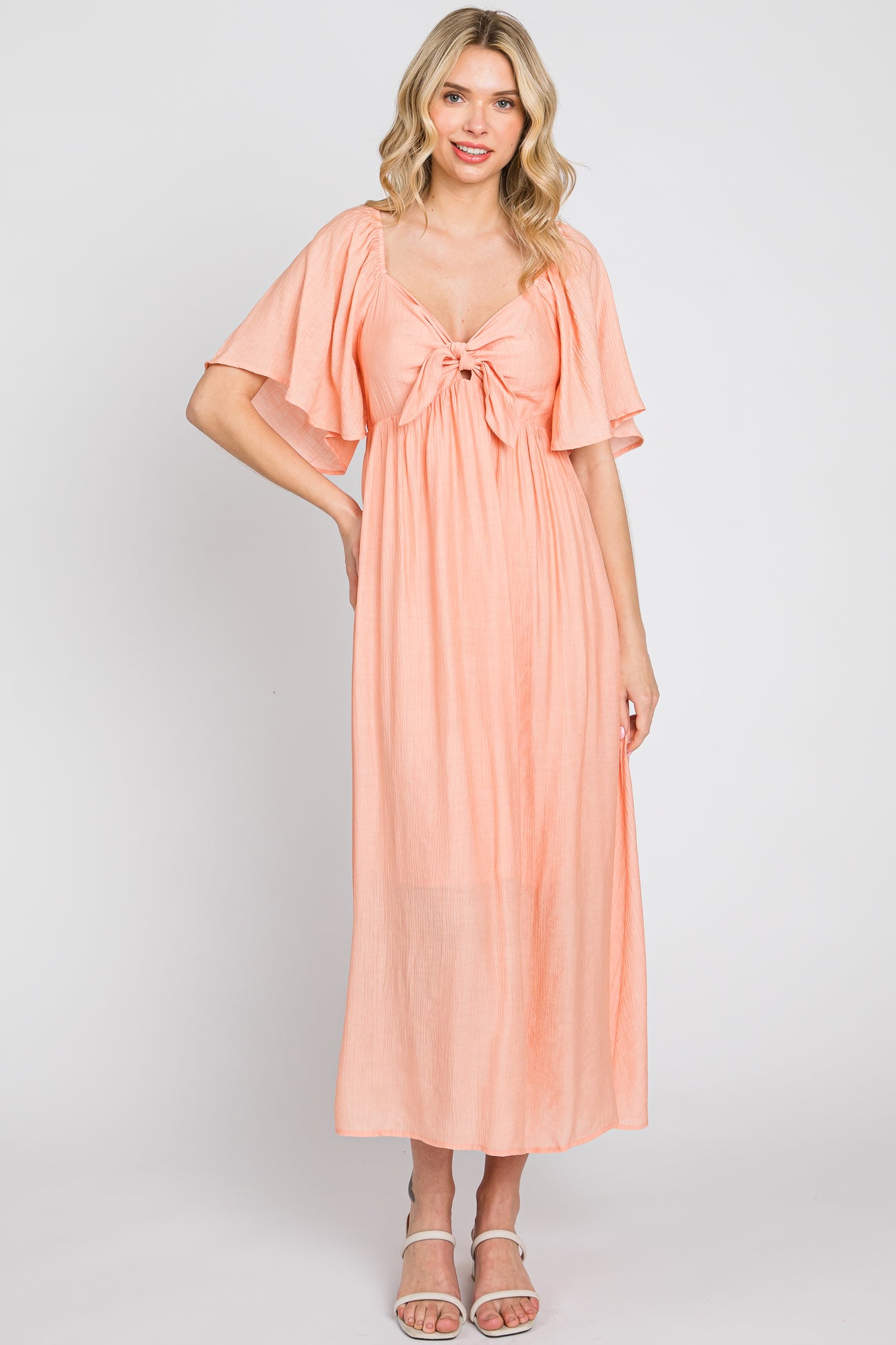 woman wearing a peach maxi dress with flutter sleeves and a tie-front detail