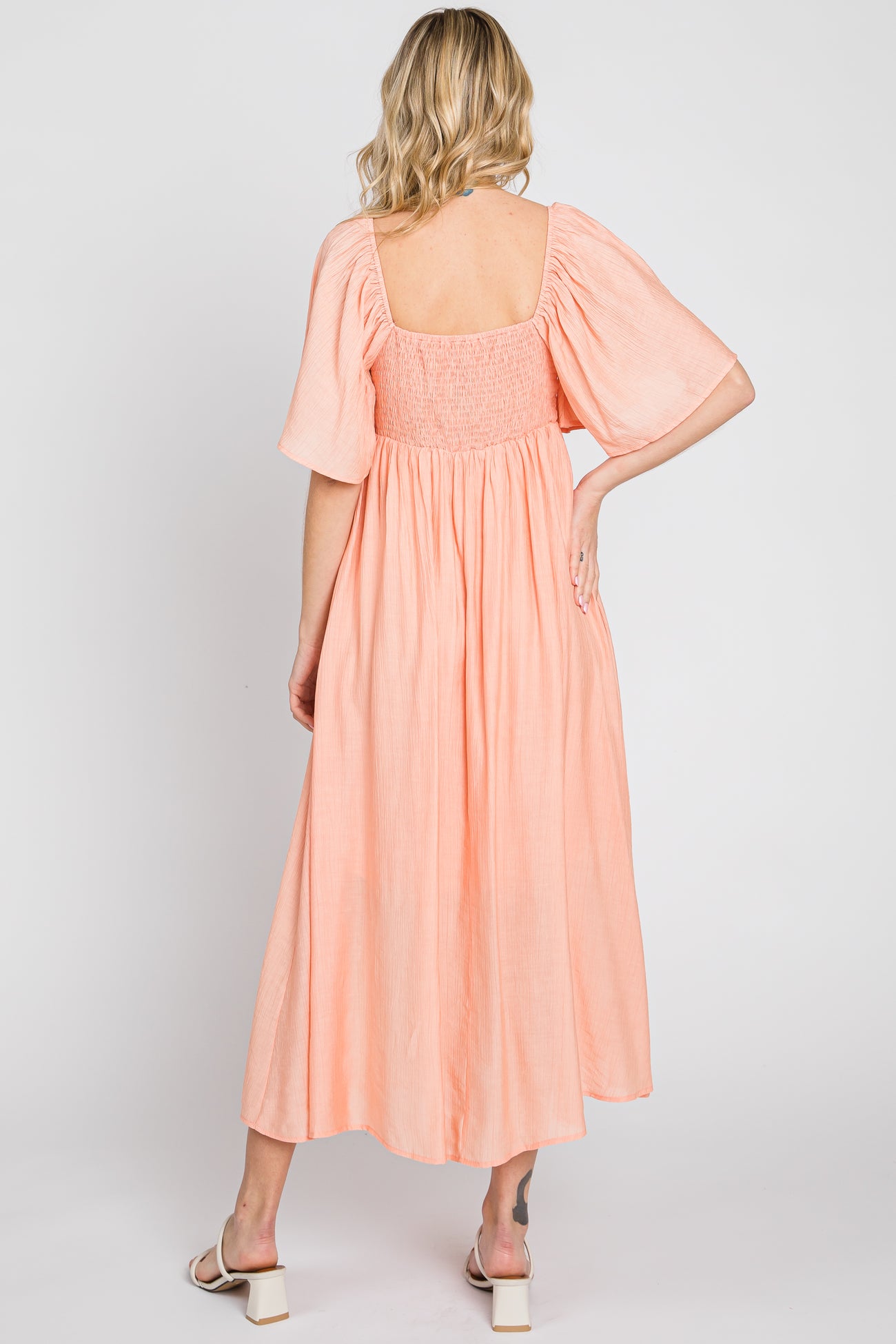 woman wearing a back view of a peach colored midi dress with puff sleeves and a smocked bodice