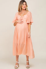 woman wearing a soft peach maternity dress with a tie front and short flutter sleeves, showcasing her baby bump