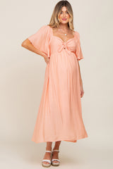 woman wearing a peach maternity maxi dress with a tie detail and flutter sleeves, showing her baby bump