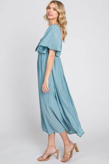 woman wearing a light blue flowing maxi dress with short sleeves and a tie waist, styled with beige sandals