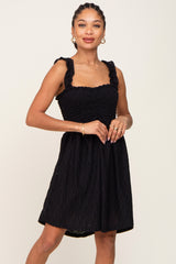 Woman wearing a black smocked eyelet mini dress with ruffle straps and gold jewelry