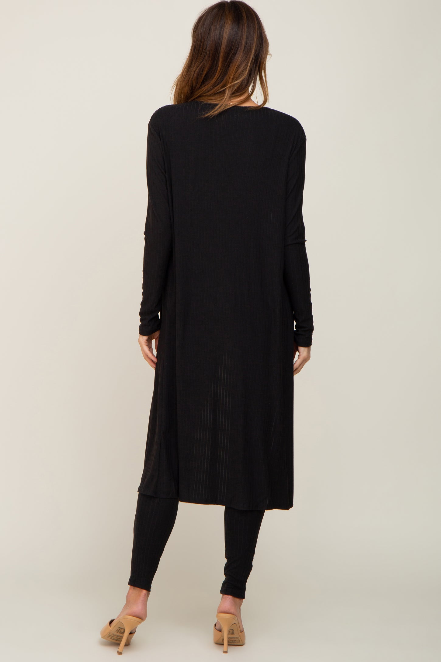 woman wearing a black long sleeve ribbed duster cardigan with side slits and matching leggings, view from the back
