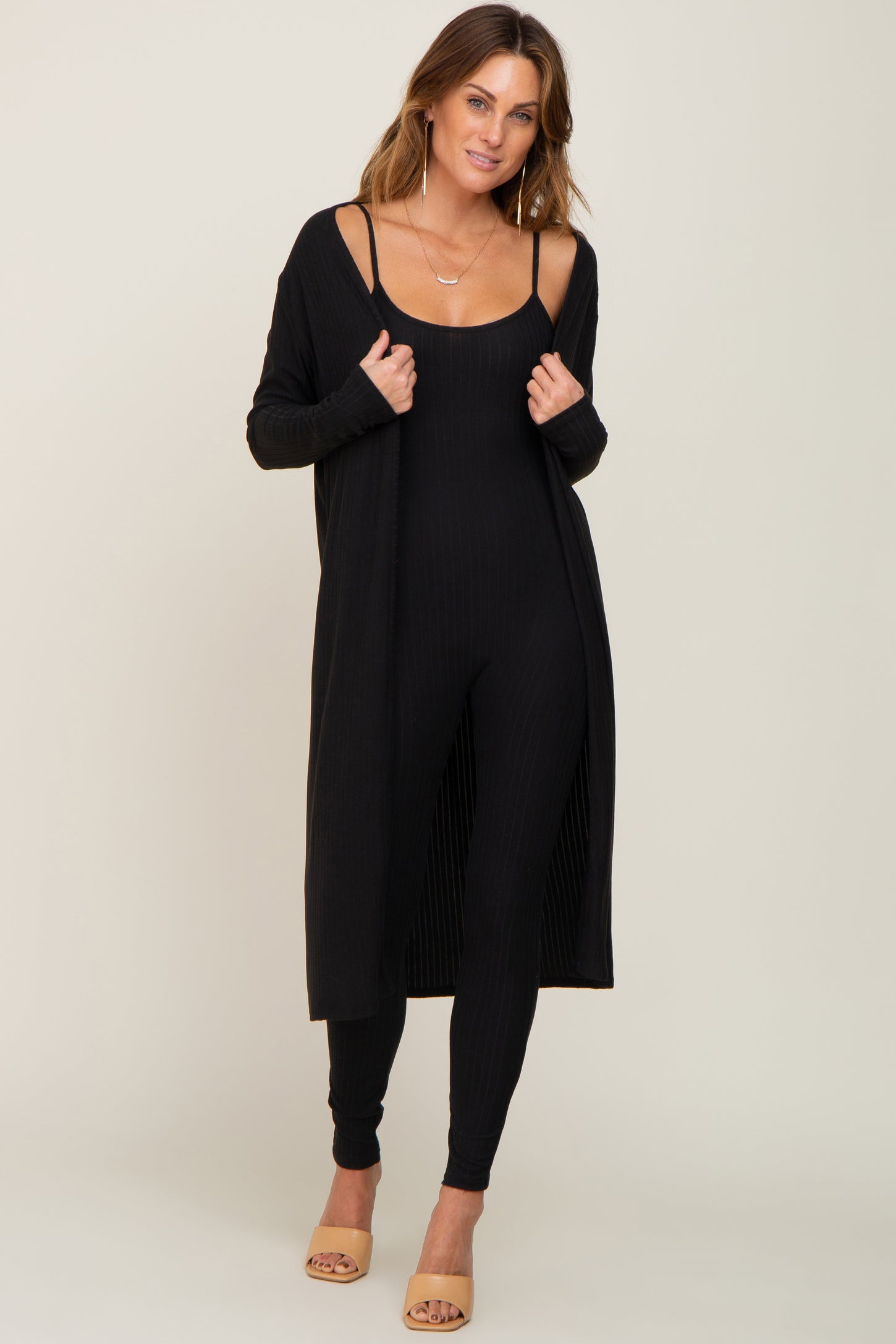 woman wearing a black ribbed jumpsuit with a matching long cardigan and heeled sandals