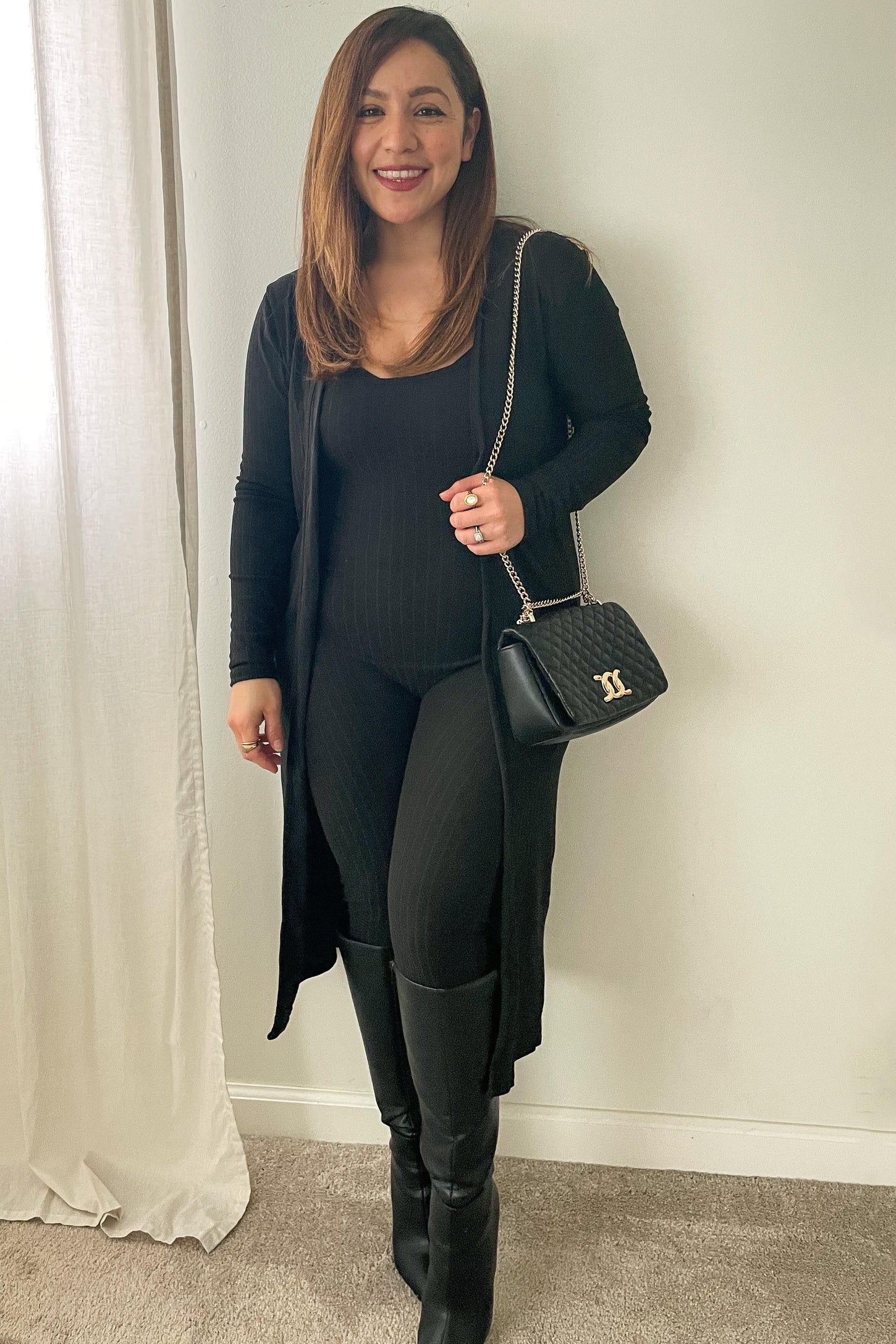 woman wearing a black ribbed bodysuit, long black cardigan, and knee-high black boots, holding a black crossbody bag