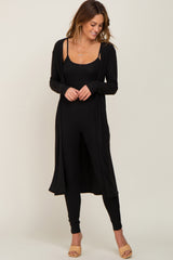 woman wearing a black ribbed long cardigan over a matching black jumpsuit and beige slide sandals
