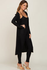 woman wearing a black ribbed long cardigan over a black ribbed jumpsuit and tan heeled mules