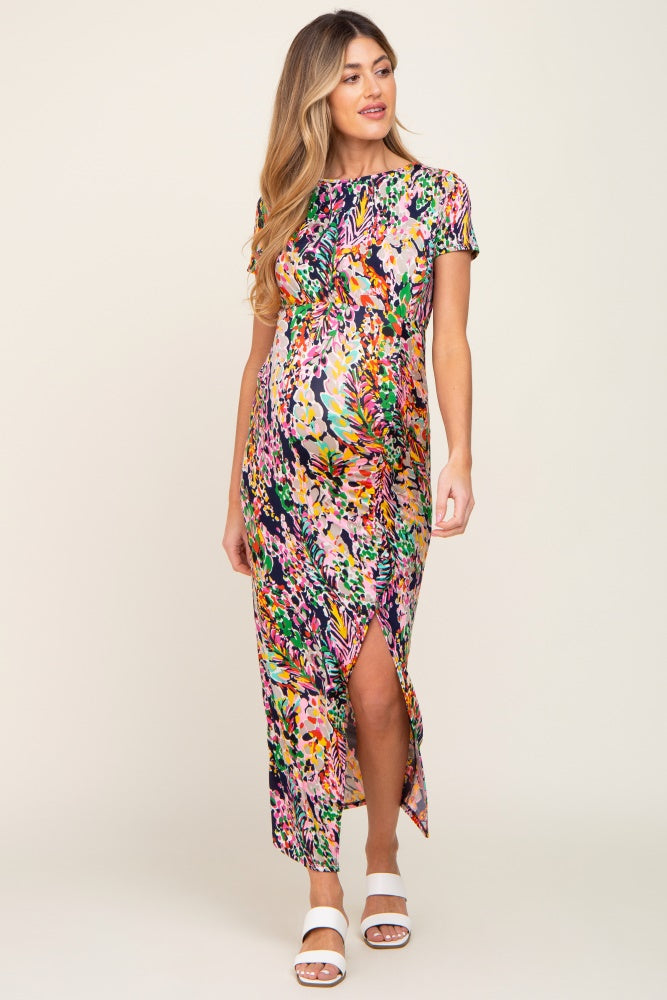 Pregnant woman wearing a multi-colored floral print maternity maxi dress with a side slit and white sandals