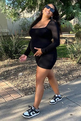 woman wearing a black long sleeve maternity dress and holding her baby bump while walking outdoors