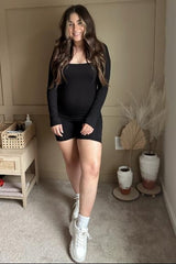 woman wearing a black long sleeve maternity dress with a visible baby bump and white sneakers