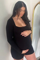 woman wearing a black long sleeve maternity top and black shorts, cradling her baby bump