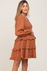 Pregnant woman wearing a rust orange smocked maternity dress with long sleeves and tiered ruffles