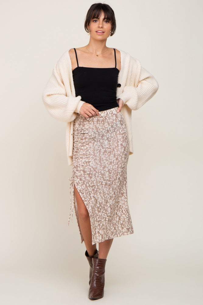woman wearing a black camisole under a cream oversized cardigan paired with a beige animal print midi skirt and brown heeled boots