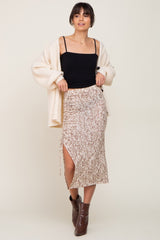 woman wearing a black spaghetti strap top with a beige animal print midi skirt and a cream cardigan, styled with brown boots