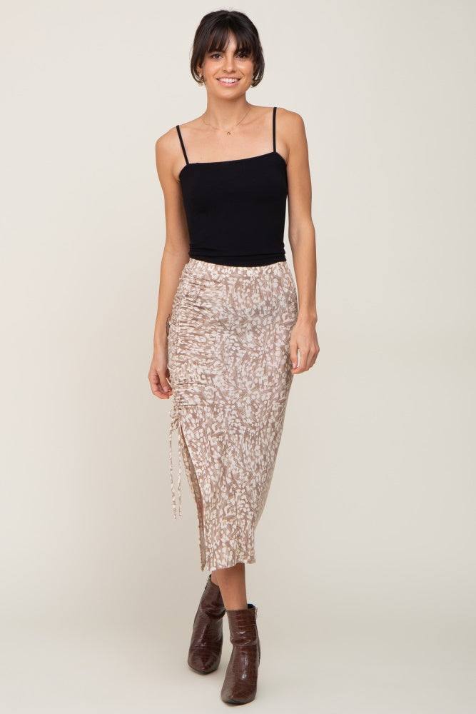 woman wearing a black spaghetti strap top and a beige animal print midi skirt with side ruching and a thigh-high slit