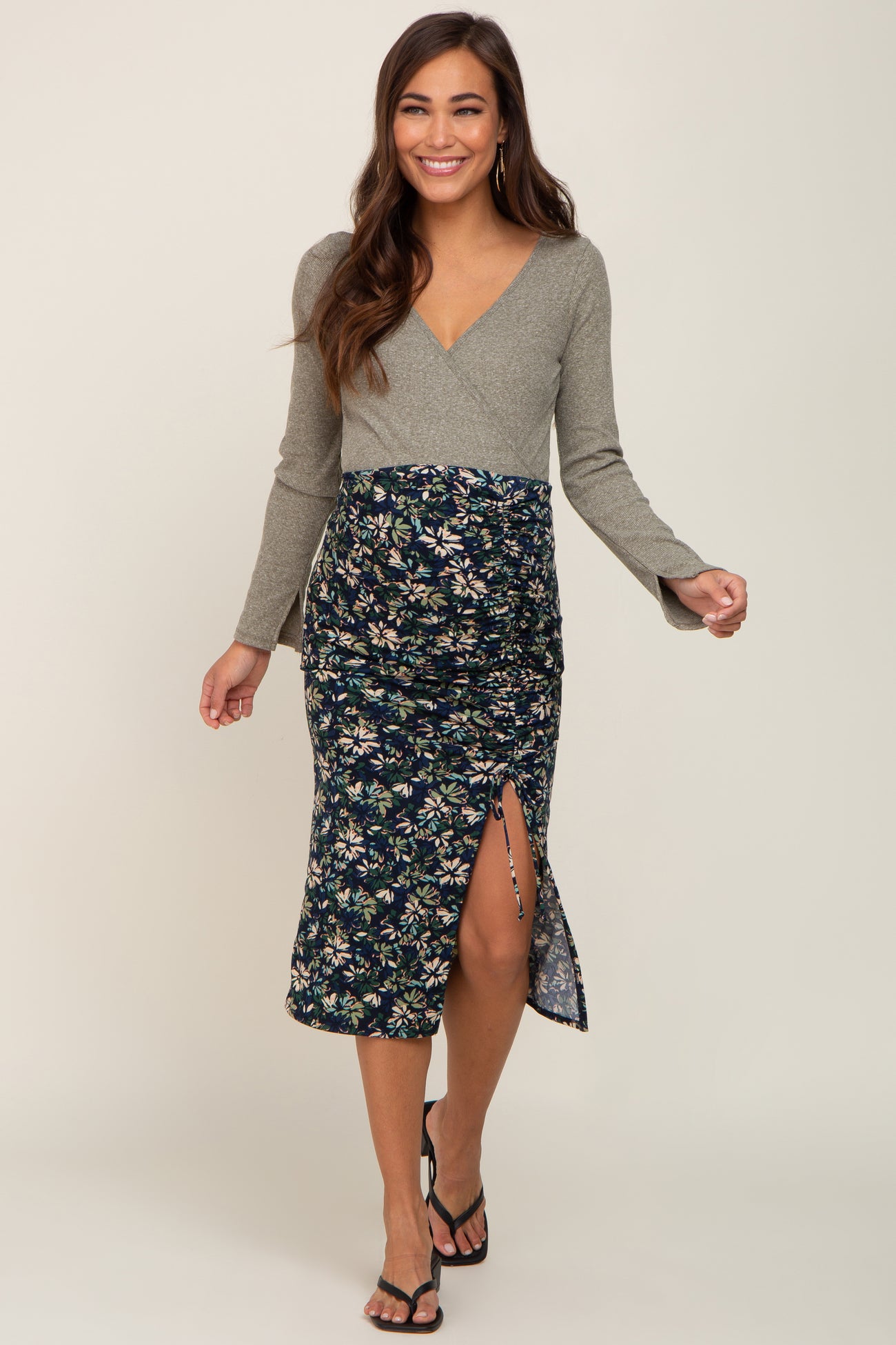 woman wearing a gray long sleeve maternity wrap dress with a floral patterned skirt and a side slit, showing her baby bump