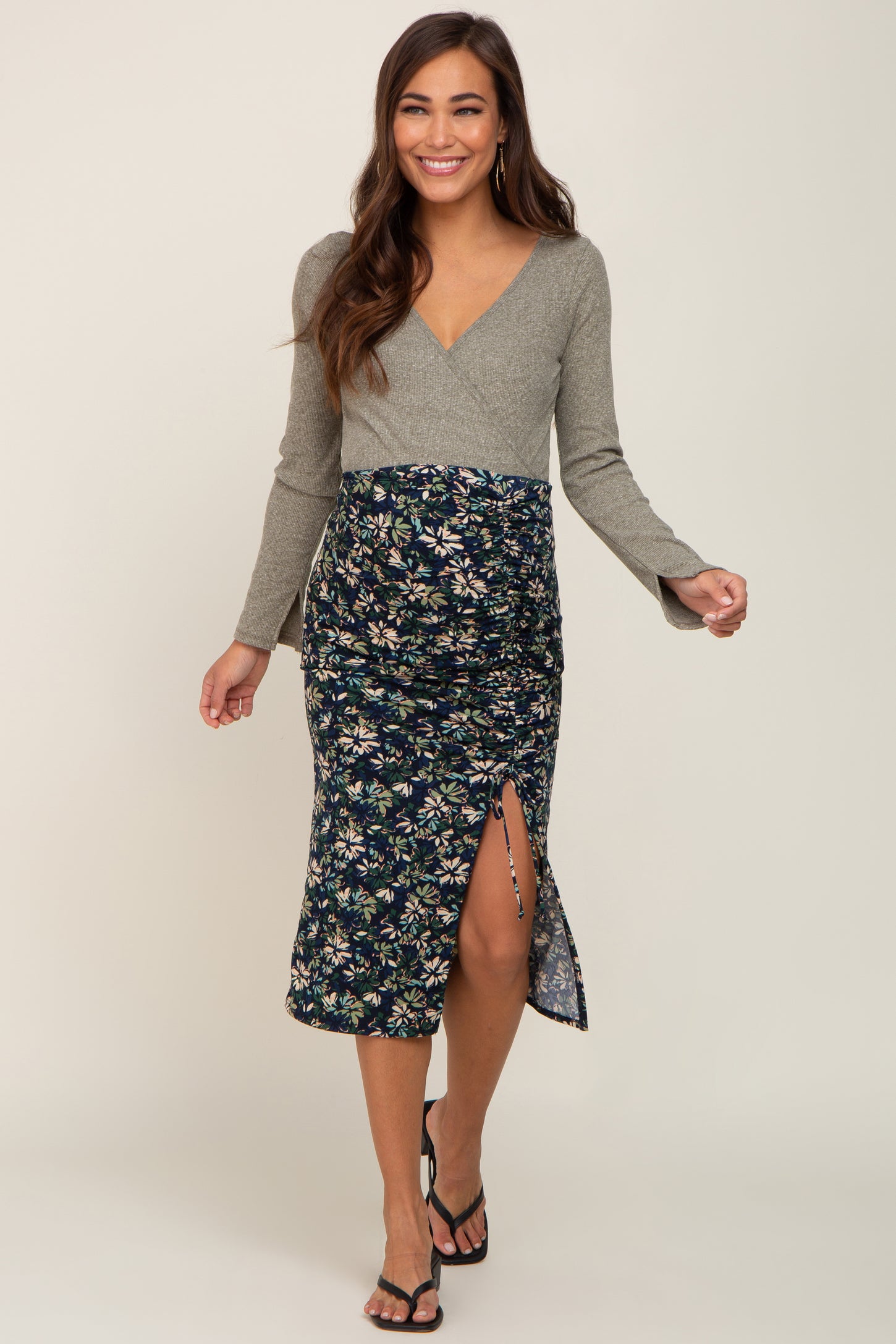 woman wearing a gray long sleeve maternity wrap dress with a floral patterned skirt and a side slit, showing her baby bump