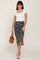 woman wearing a white short sleeve crop top and a floral midi skirt with a side slit, holding a brown handbag