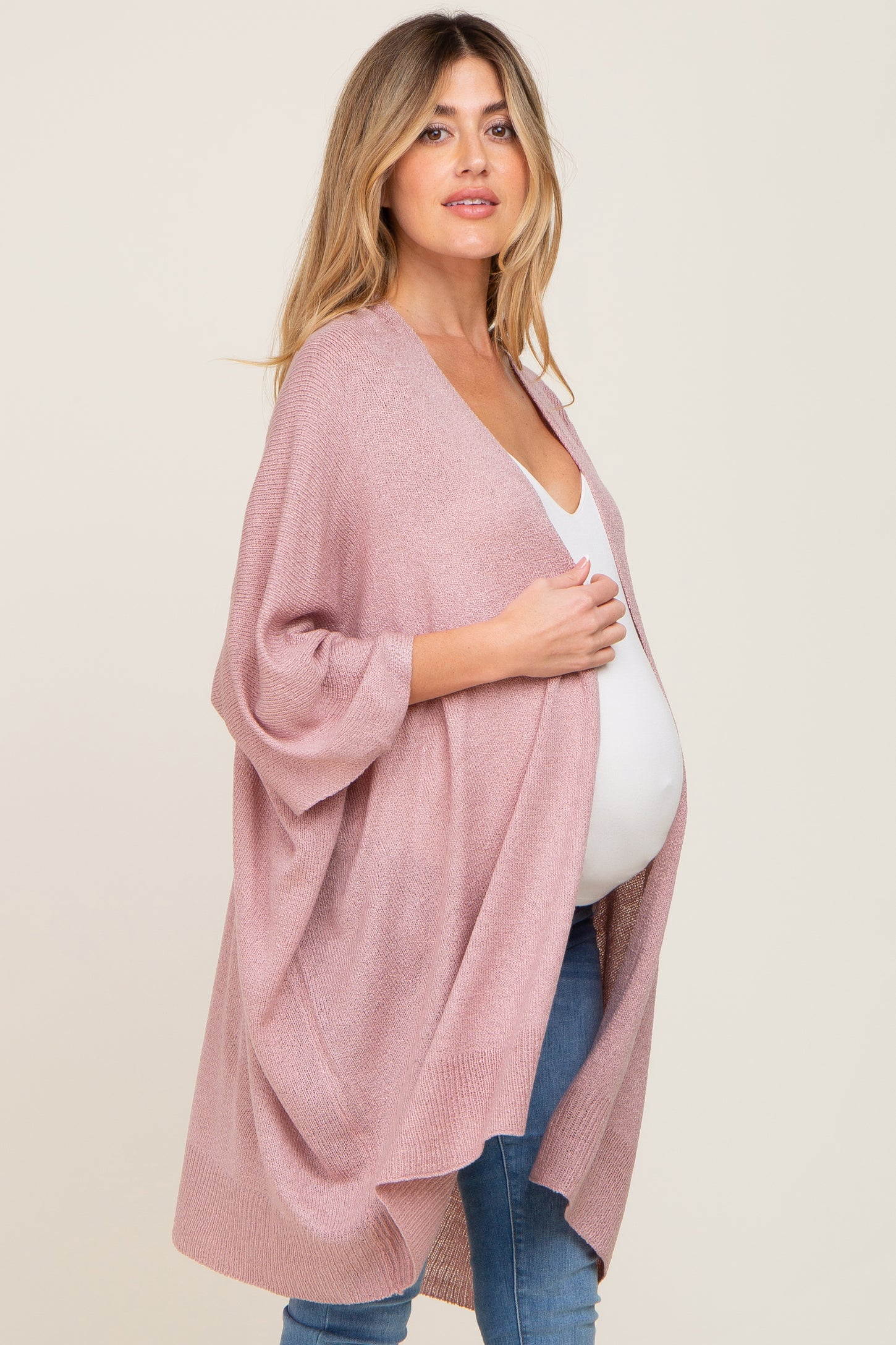 Pregnant woman wearing a mauve oversized knit maternity cardigan over a white top and blue jeans
