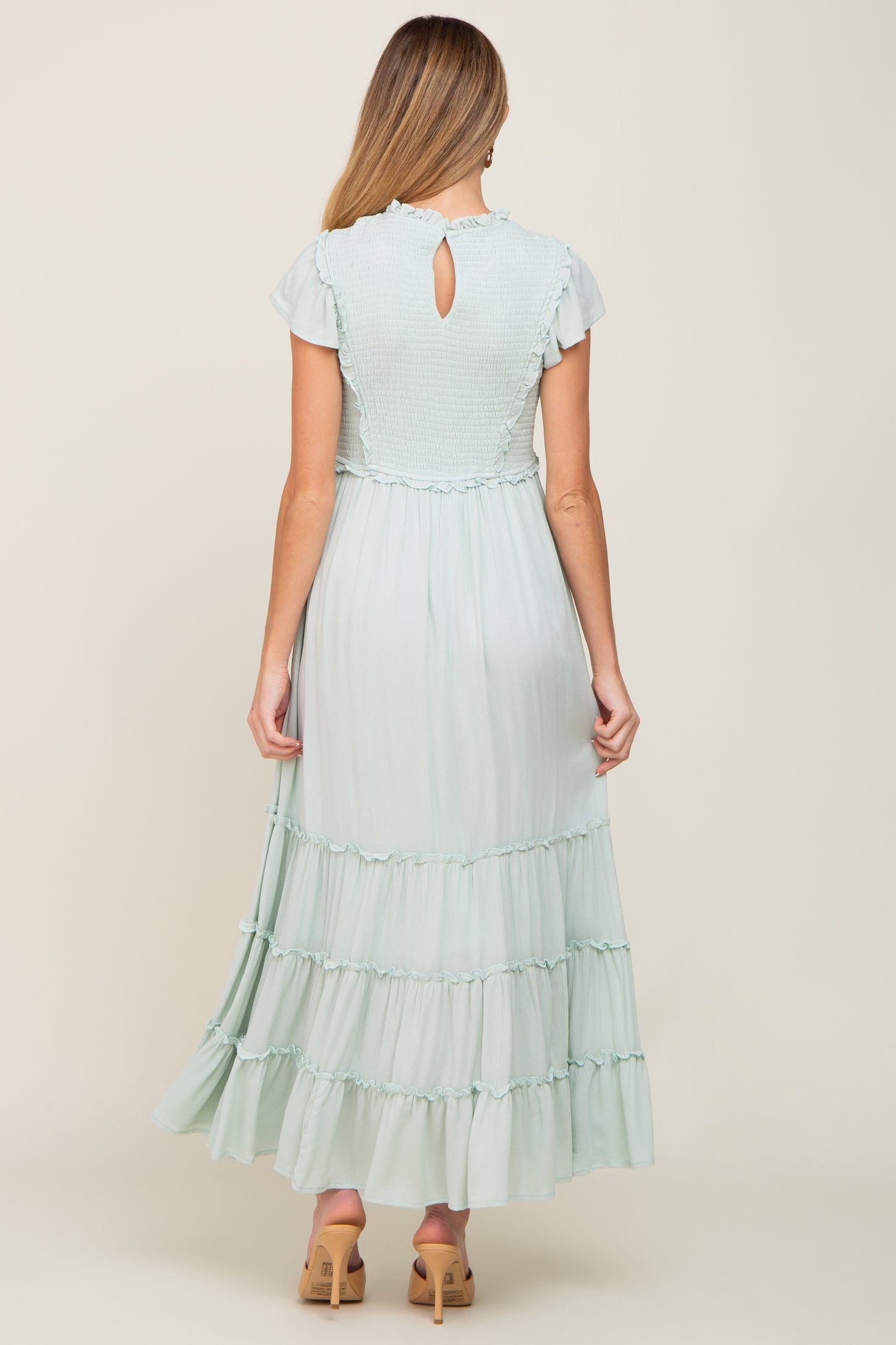 Back view of a woman wearing a light sage green smocked maxi dress with ruffled tiers and short flutter sleeves