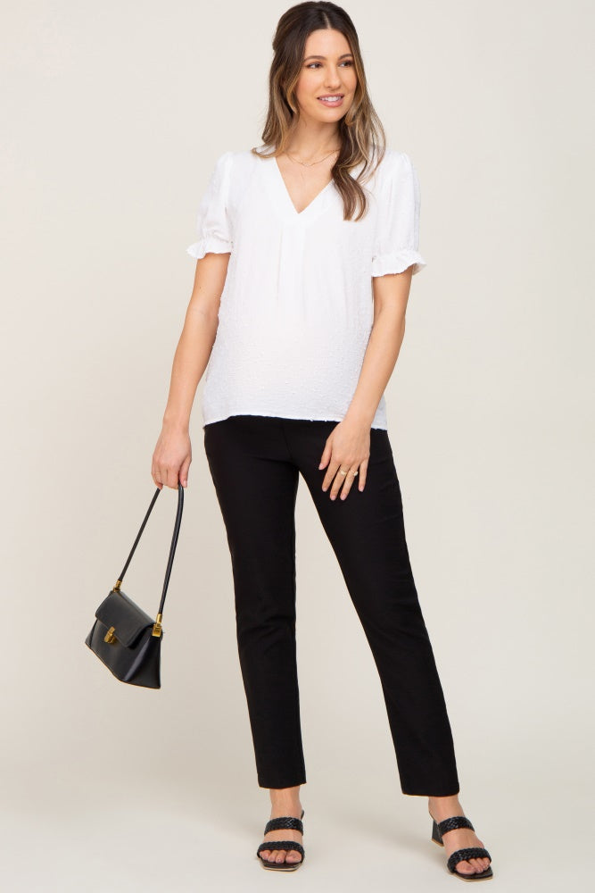 woman wearing a white maternity top with puff sleeves, paired with black pants and holding a black handbag