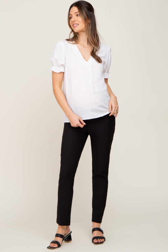 woman wearing a white short sleeve maternity top and black fitted pants with a visible baby bump