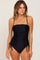 woman wearing a black one-piece swimsuit with ruched sides and thin straps against a neutral background