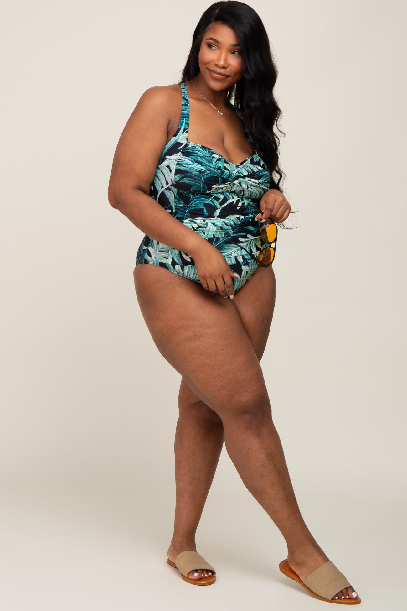 woman wearing a tropical print plus size swimsuit with adjustable straps and ruched detailing, styled with sandals and sunglasses