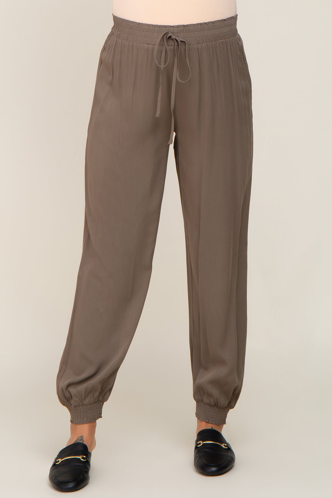 woman wearing taupe jogger pants with drawstring waist and elastic cuffs paired with black loafers