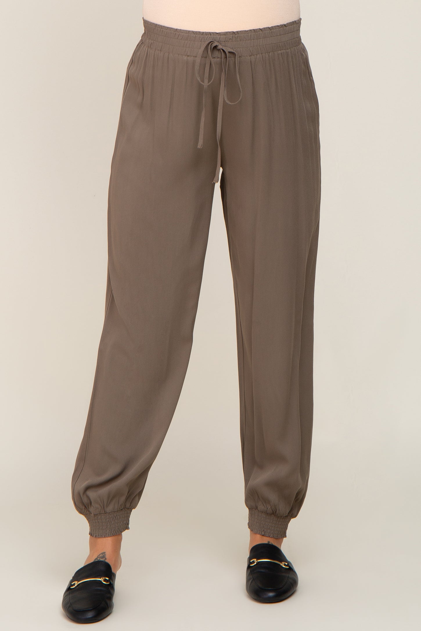 woman wearing taupe jogger pants with drawstring waist and elastic cuffs paired with black loafers