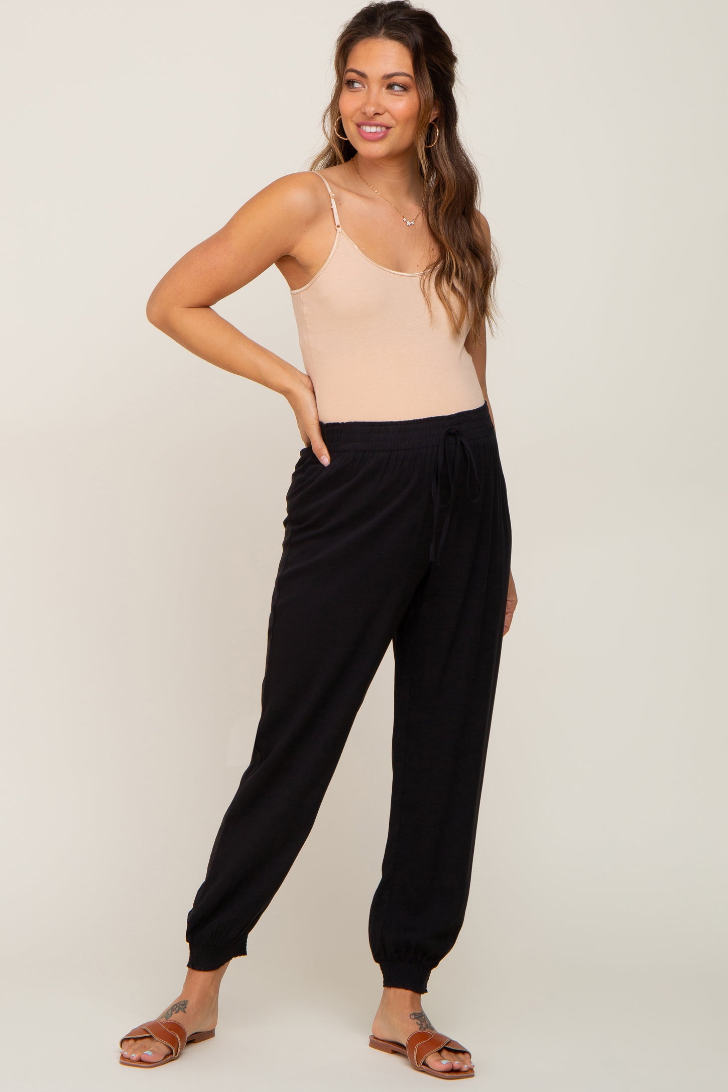 woman wearing a beige maternity bodysuit and black maternity jogger pants with elastic cuffs and drawstring waist