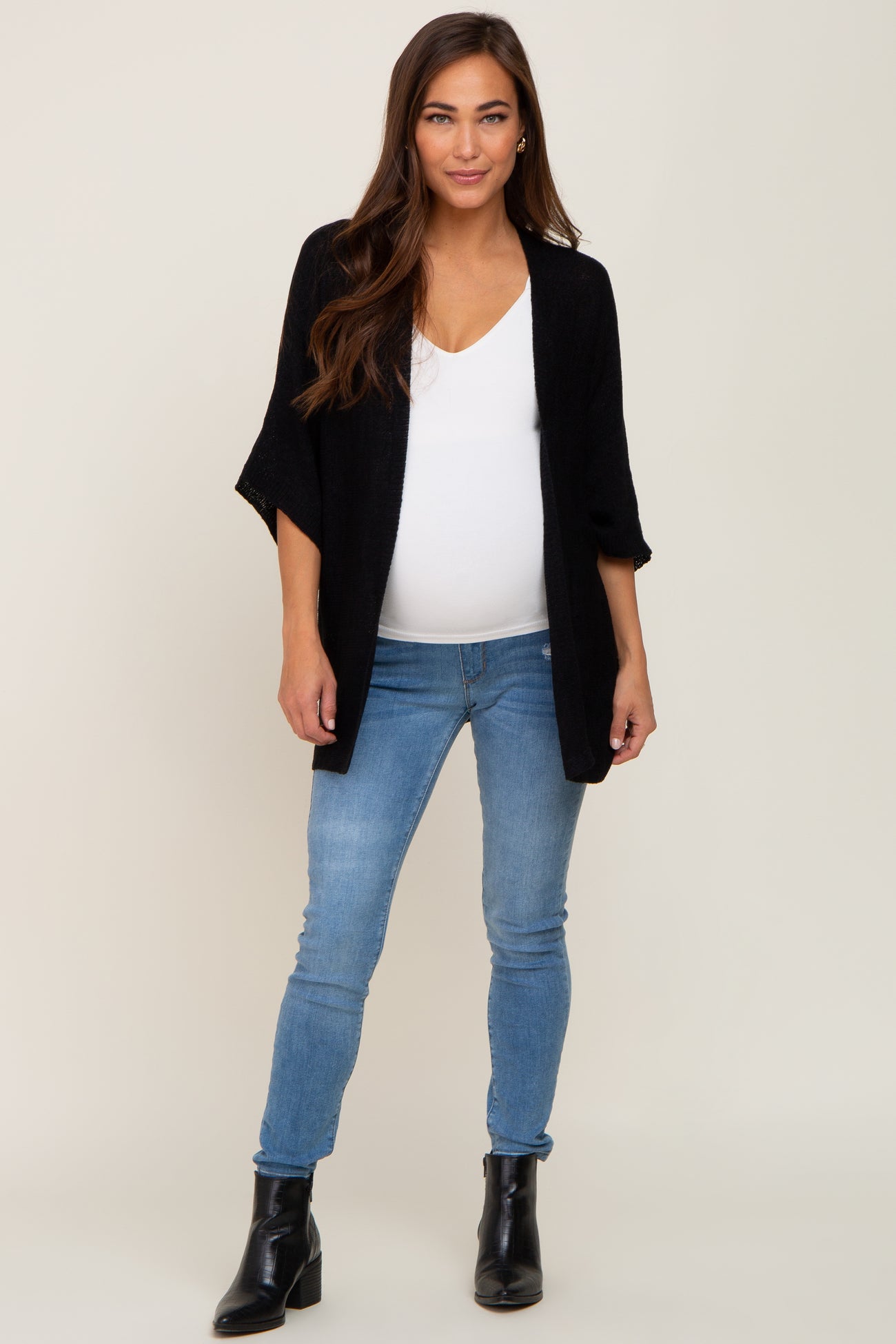 woman wearing a black open-front cardigan with a white v-neck top and jeans, showcasing her baby bump