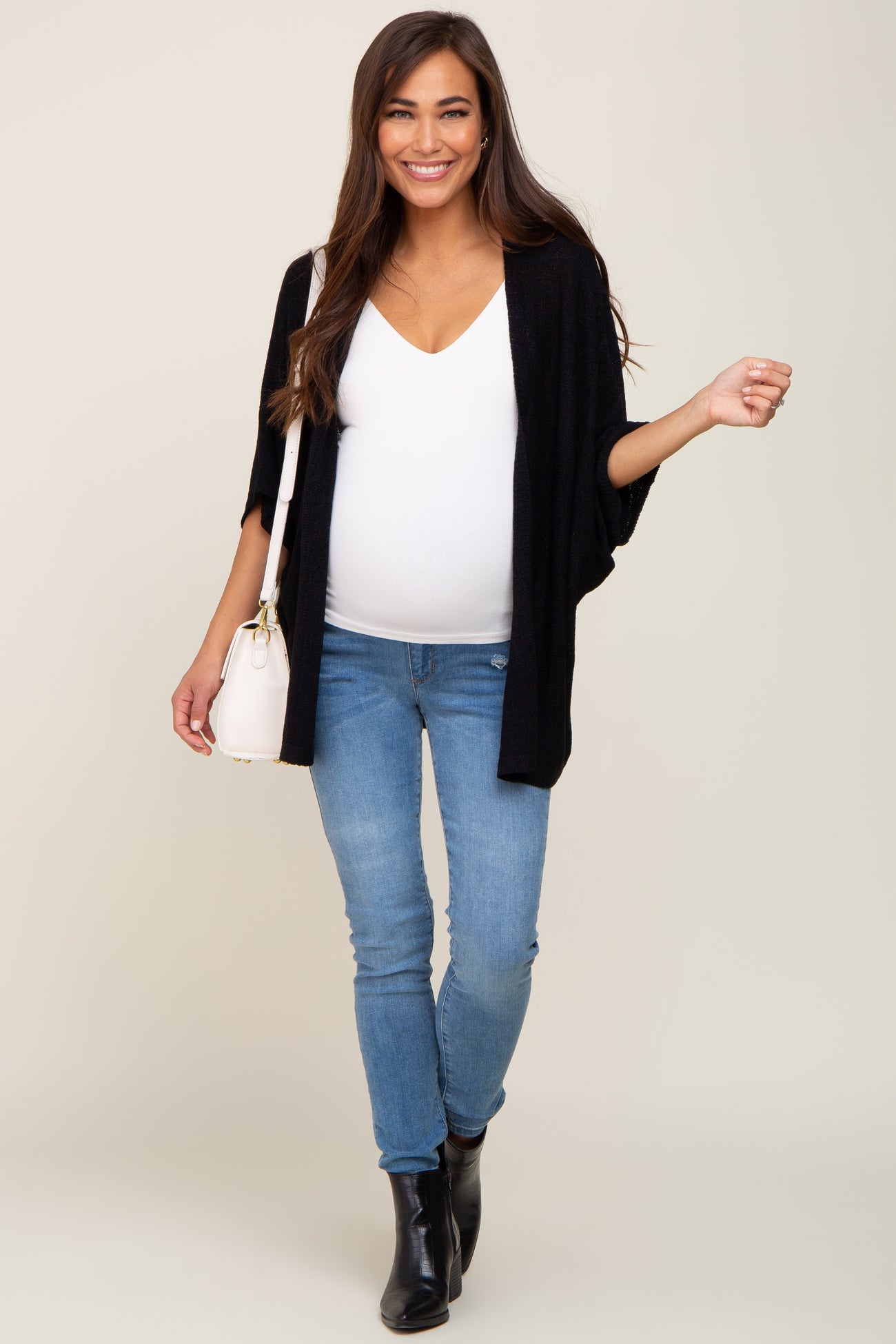 woman wearing a black kimono cardigan, white v-neck top, and blue skinny jeans, showing her baby bump