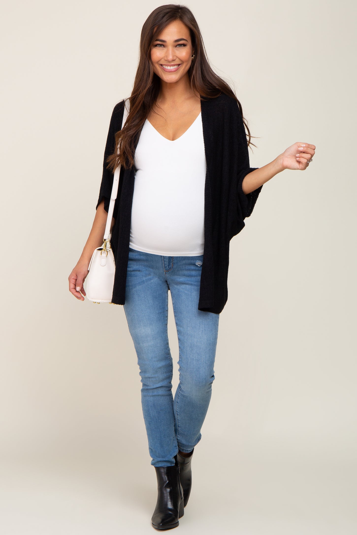 woman wearing a black kimono cardigan, white v-neck top, and blue skinny jeans, showing her baby bump