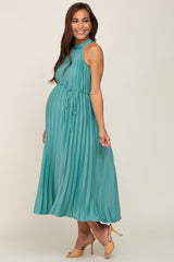 pregnant woman wearing a teal pleated halter maternity midi dress with a waist tie and tan heels
