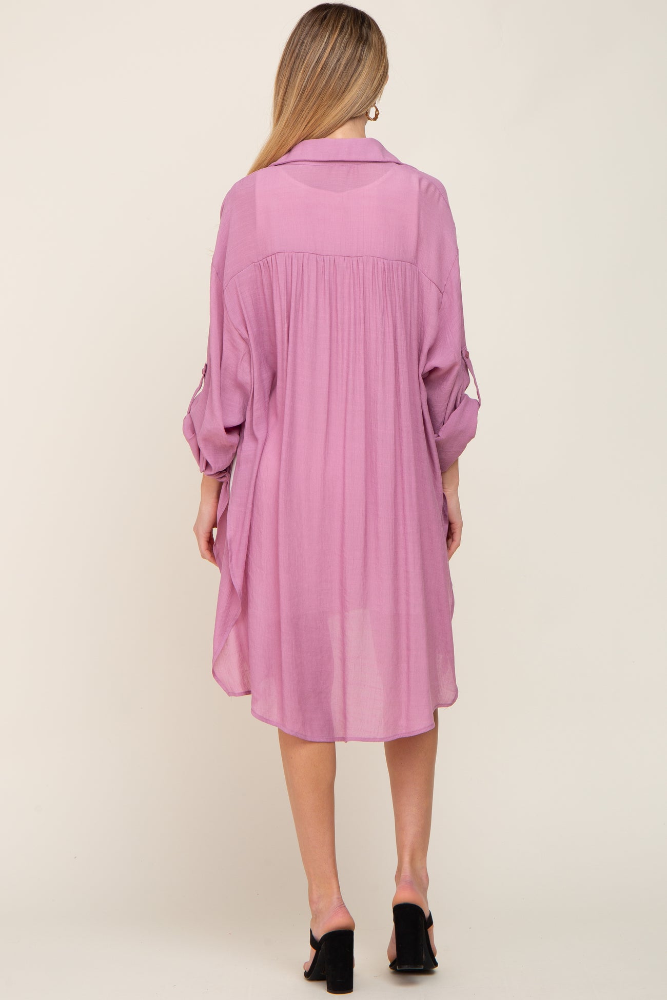 Back view of a woman wearing a mauve oversized button-down tunic dress with rolled sleeves and black heels