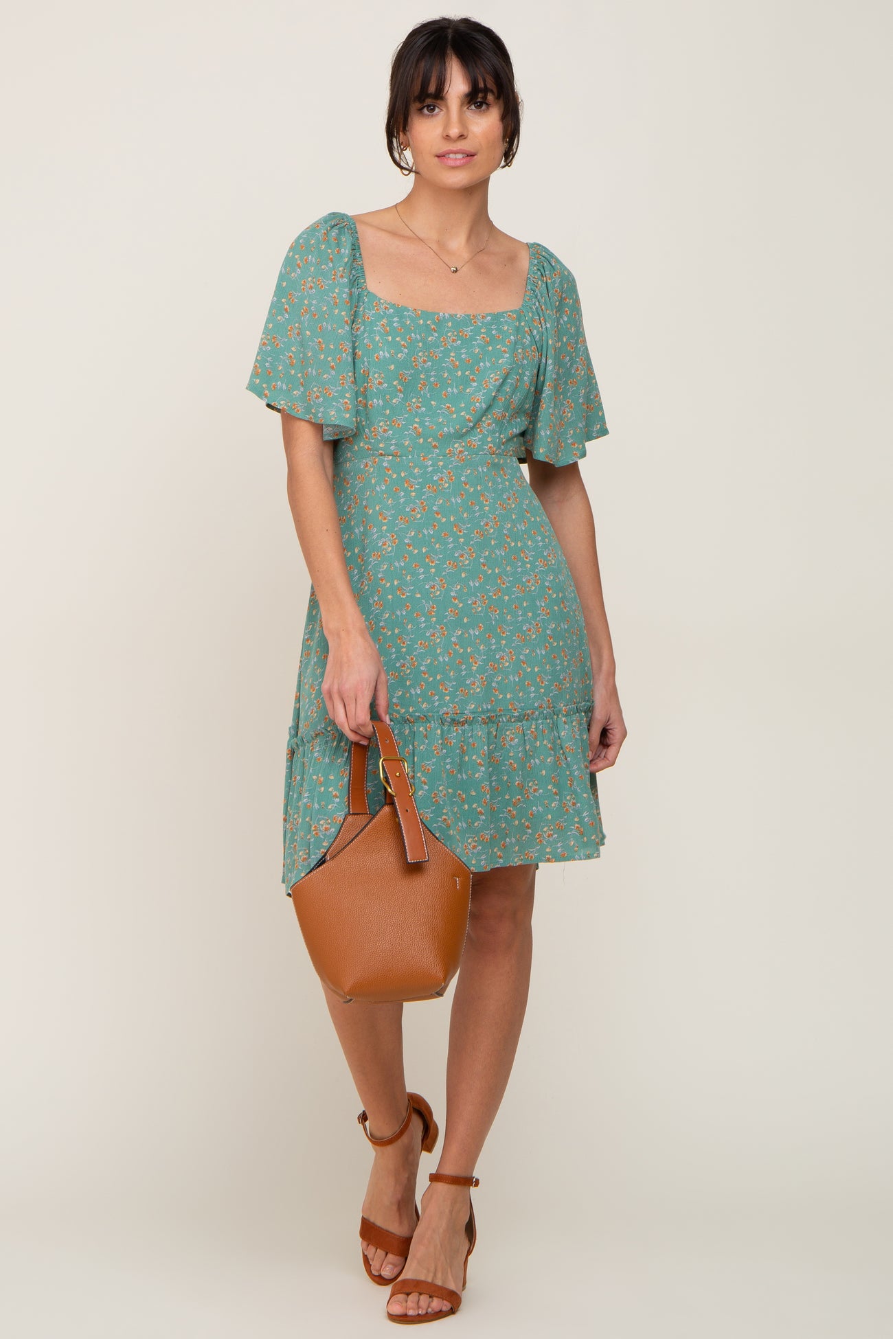woman wearing a green floral mini dress with flutter sleeves and holding a brown leather handbag