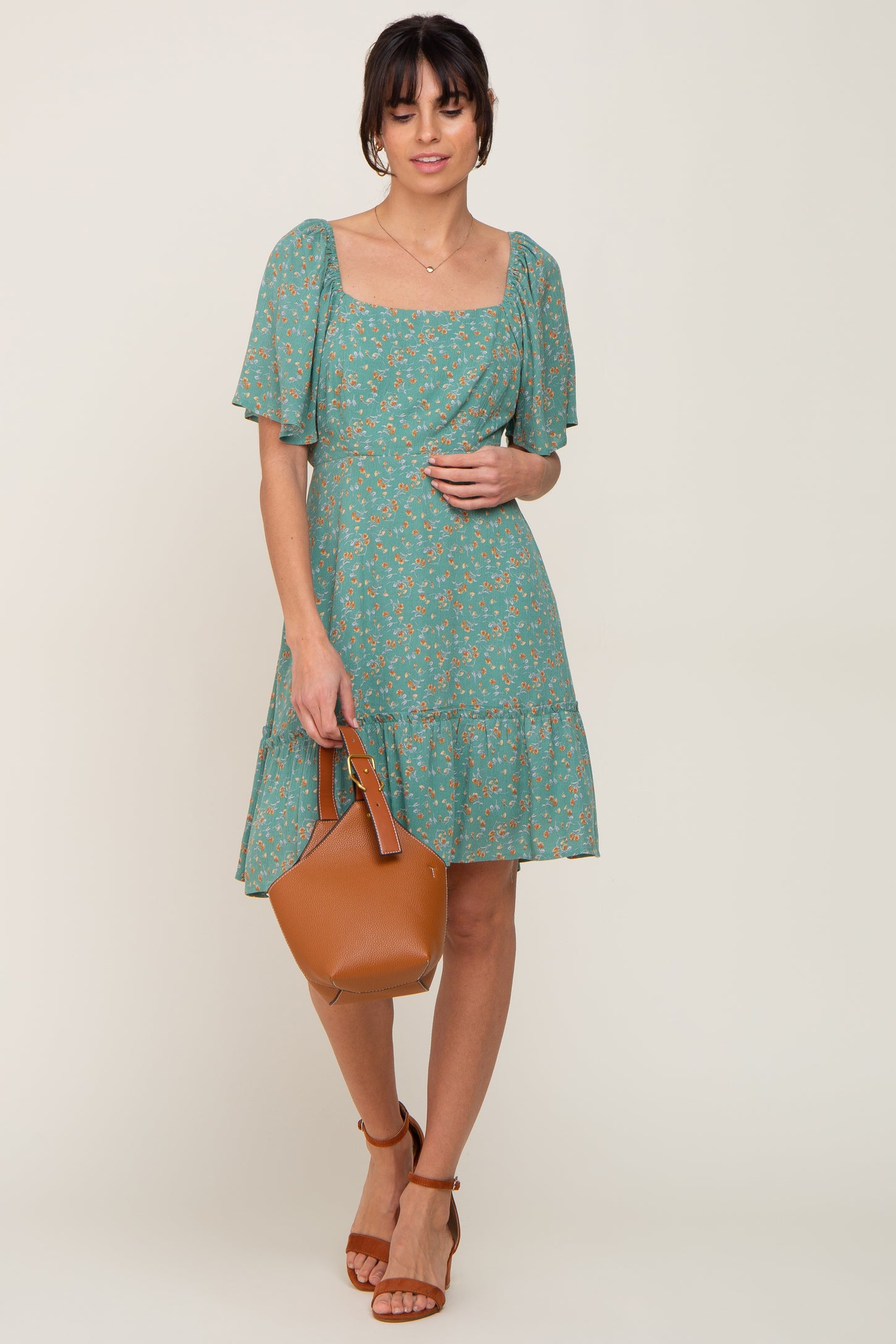 woman wearing a green floral square neck mini dress with short puff sleeves and holding a brown leather handbag