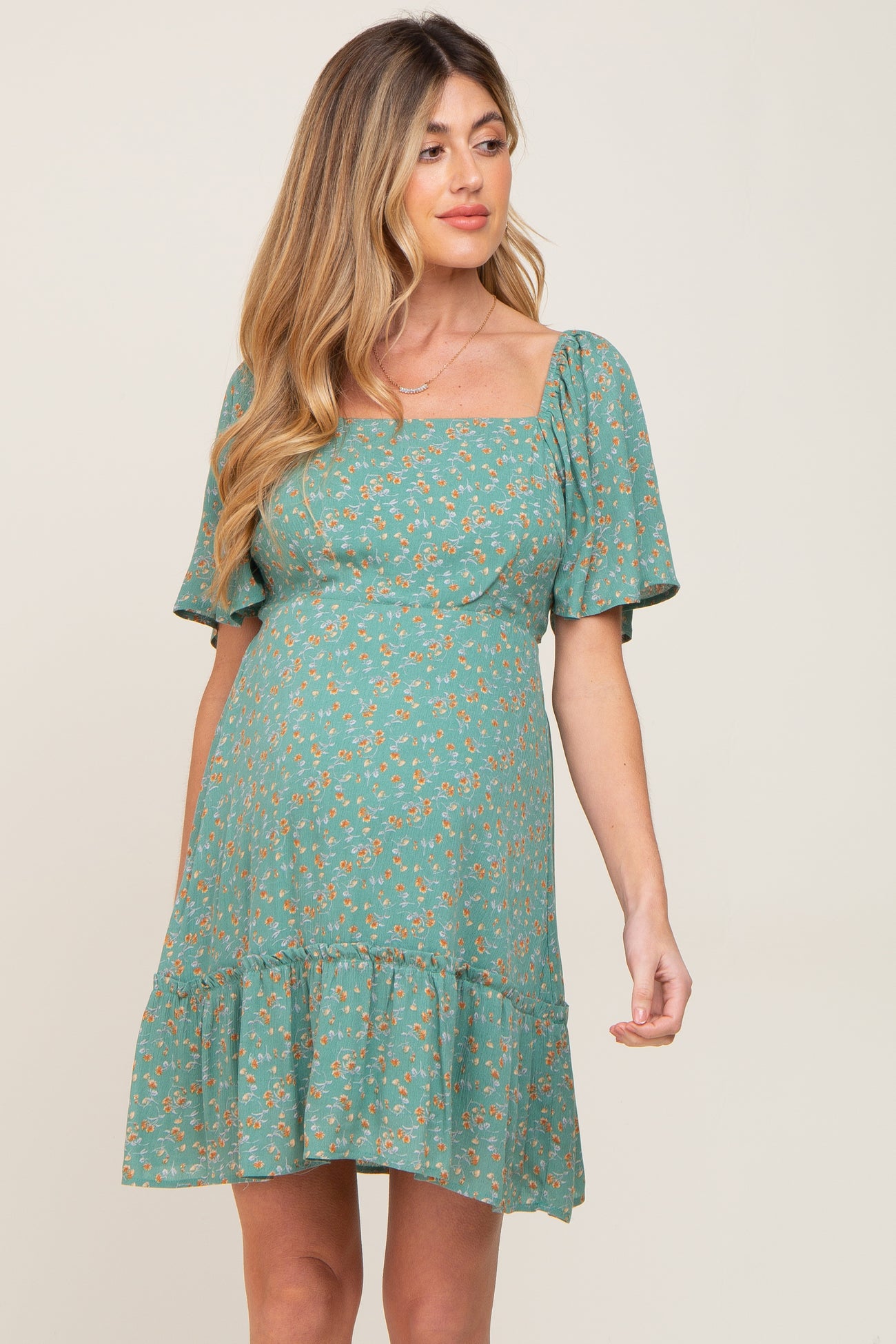 pregnant woman wearing a green floral maternity dress with a square neckline and short puff sleeves