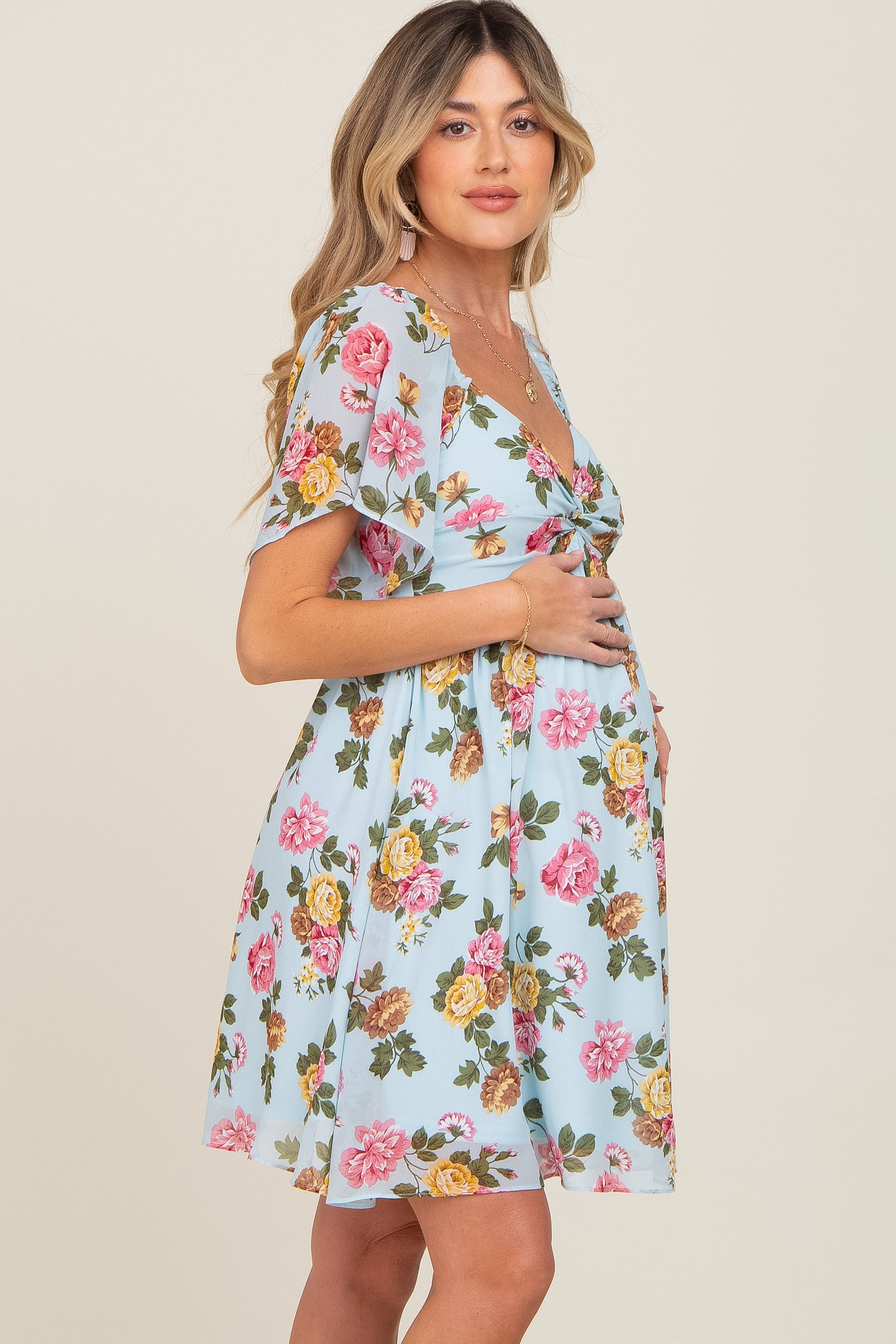 Pregnant woman in light blue floral maternity mini dress with flutter sleeves holding her baby bump