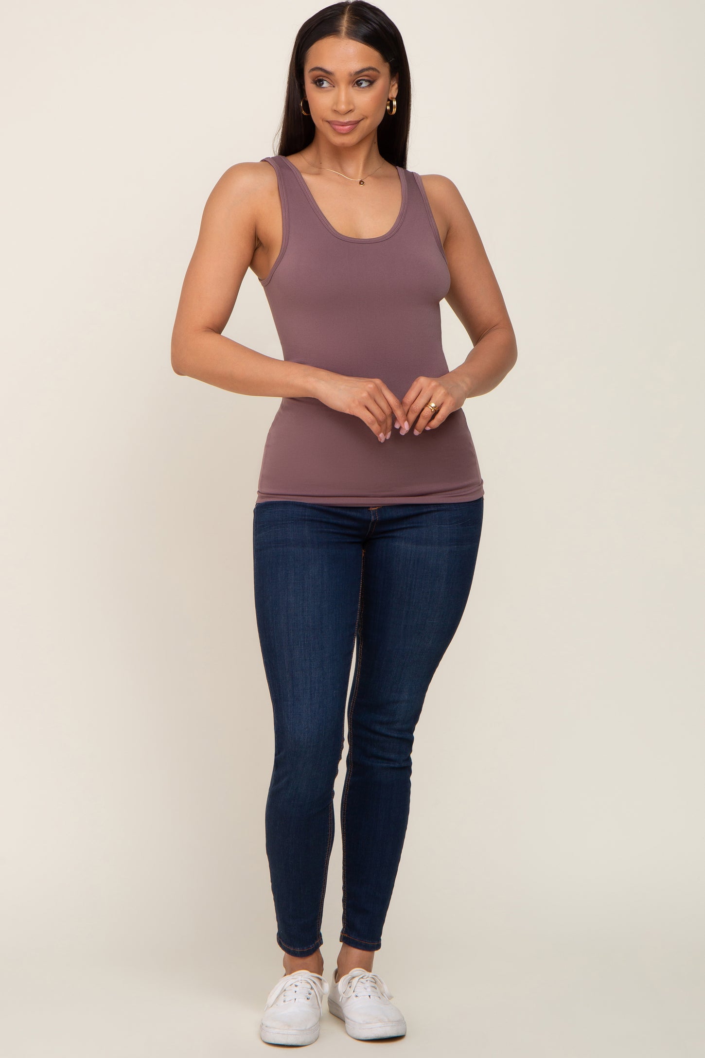 woman wearing a mauve racerback tank top with blue skinny jeans and white sneakers
