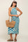 woman wearing a blue and white patterned halter neck midi dress and holding a woven straw bag