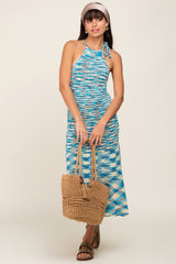 woman wearing a blue and white knit halter dress, holding a woven tote bag and wearing a headband