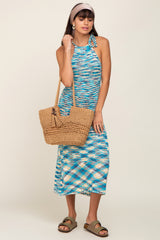 Woman in blue and white space-dye halter midi dress holding a woven straw tote bag with tassel detail