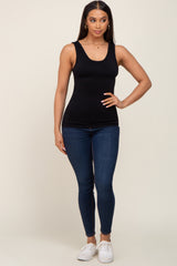 woman wearing a fitted black tank top and skinny blue jeans, standing with one hand on her hip