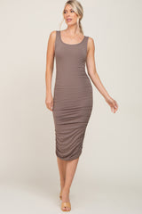 woman wearing a taupe sleeveless ruched midi dress with a scoop neckline and a bodycon fit
